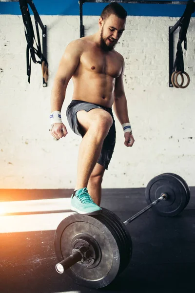 Ung man förbereda för skivstångsträning i gymmet. sätta sitt ben på skivstång — Stockfoto