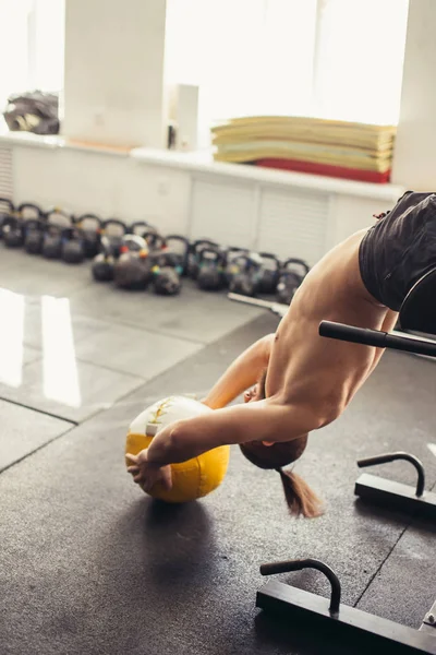 Чоловік сидить на лавці з медичним м'ячем, працює над м'язами живота — стокове фото