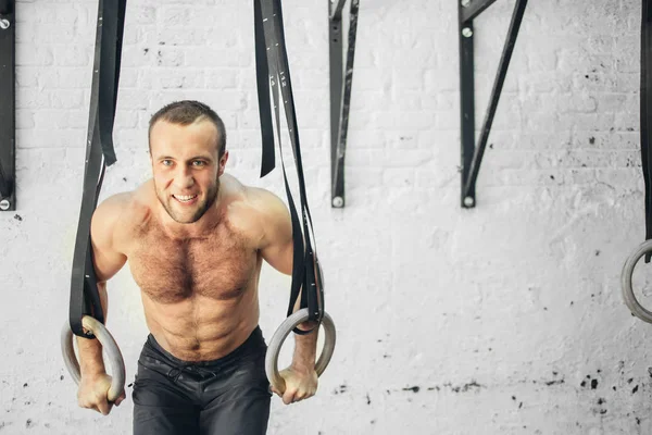 fit man pulling up on gymnastic rings.