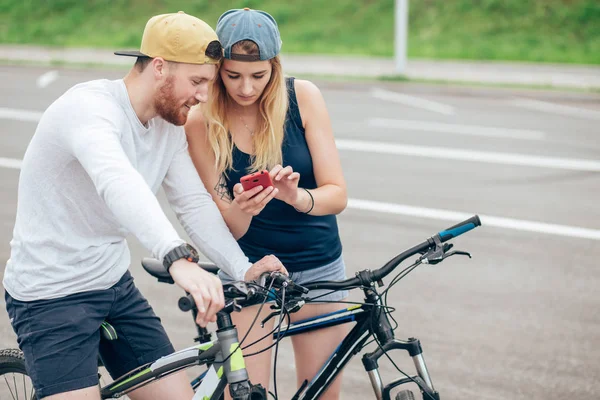Jeune couple joyeux à vélo regardant dans le téléphone intelligent, télécharger des photos prises — Photo