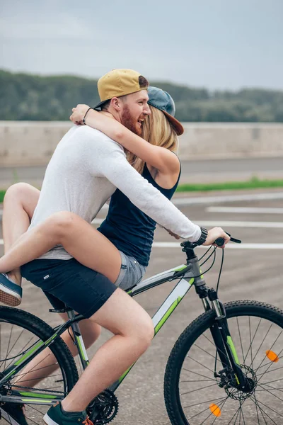 Homem feliz dando namorada um elevador em sua barra de bicicleta na praia — Fotografia de Stock