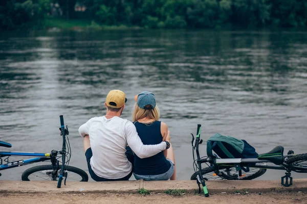Romantyczna para z rowerami relaksujący na zachód słońca nad jeziorem. Zakochać się w pojęcie miłości. — Zdjęcie stockowe