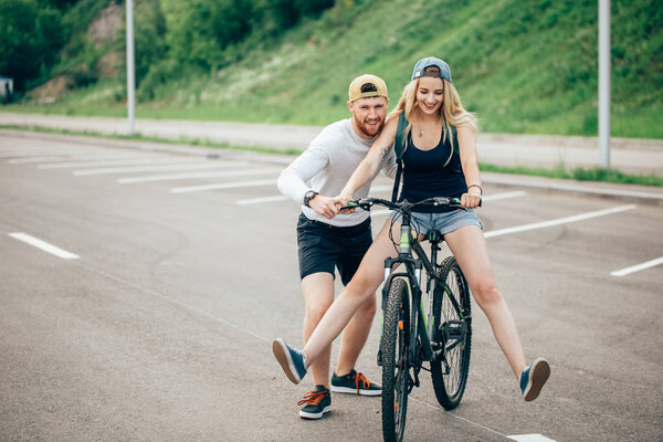 Девушка на велосипеде, парень бежит. Мальчик учит девочку кататься на велосипеде. Утренний луг
.