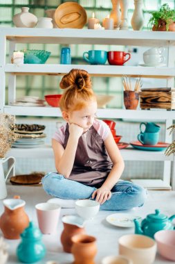 birçok fincanla kil atölye stüdyoda oturan Kızıl saçlı kız