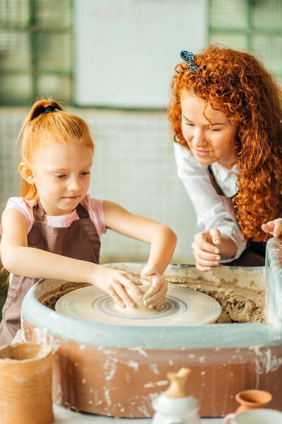 redhead mother and her child daughter moulding with clay on pottery wheel