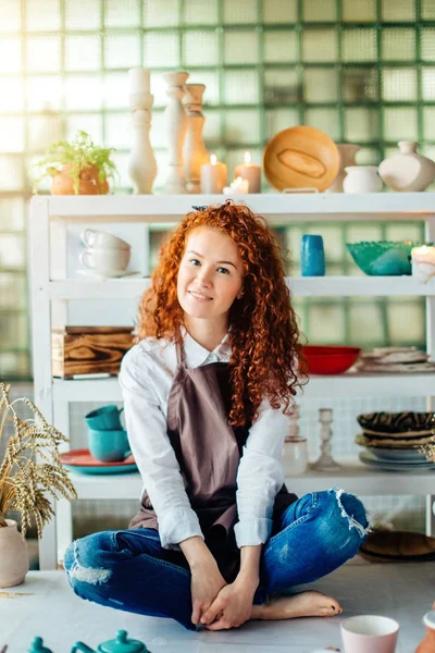 Redhead woman sitting in lotus pose in clay shop — Stock Photo, Image