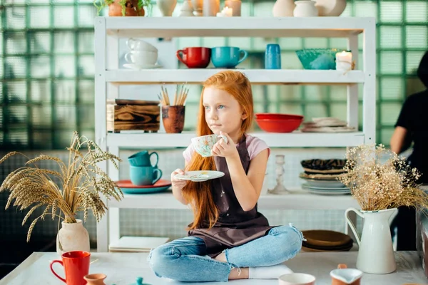 Rothaarige Mädchen, die in Lotus-Pose im Studio sitzen, bestehen aus Keramiktassen — Stockfoto