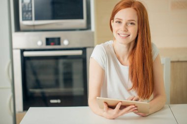Tablet tutarak ve kameraya bakarak mutlu genç kadın