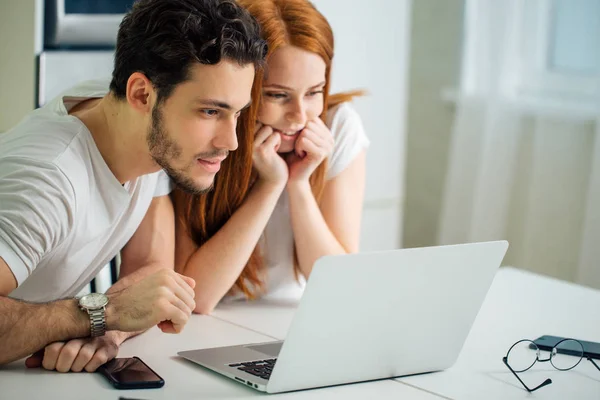 Paar, das gemeinsam am Tisch im Internet surft, lächelt und liest Bildschirm — Stockfoto
