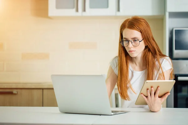 Fêmea trabalhando online com tablet digital e laptop enquanto está sentada à mesa — Fotografia de Stock