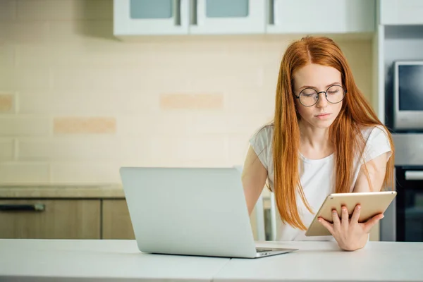 Redhead using the tablet pc and laptop in kitchen — Stock Photo, Image
