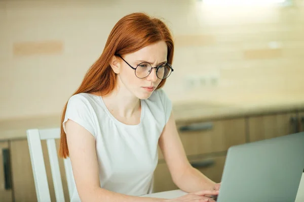 Концентрированная рыжая деловая женщина, работающая на ноутбуке в ярком современном офисе — стоковое фото
