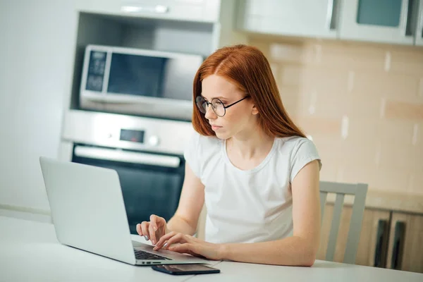 Femeie de afaceri roșcată concentrată care lucrează pe laptop într-un birou modern luminos — Fotografie, imagine de stoc
