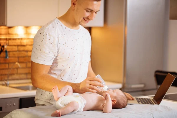 dad trying to work while standing with his newborn babe in home office interior