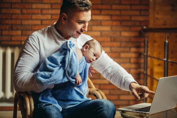 Чоловік працює за столом вдома з ноутбуком, тримає милих немовлят, дивлячись на екран — стокове фото