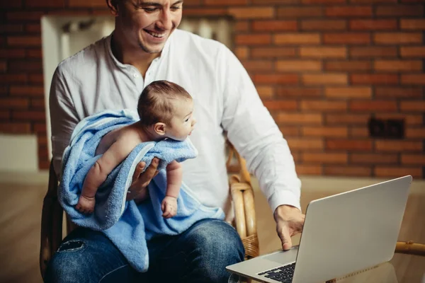 Чоловік працює за столом вдома з ноутбуком, тримає милих немовлят, дивлячись на екран — стокове фото
