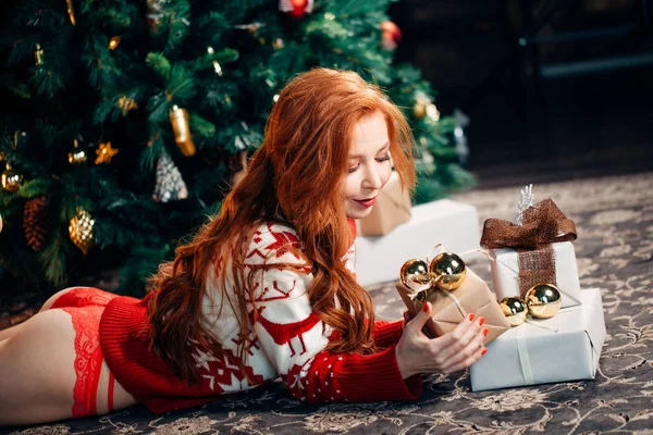 Sexy meisje in de rode ondergoed en trui liggen in de buurt van de kerstboom en open cadeau — Stockfoto