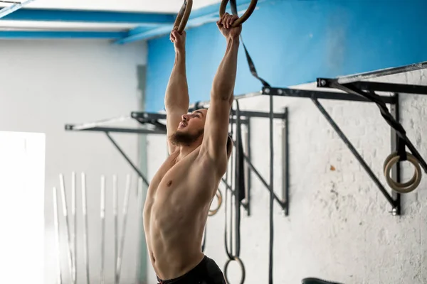 Muscle-up exercise athletic man doing intense workout at gym on gymnastic rings