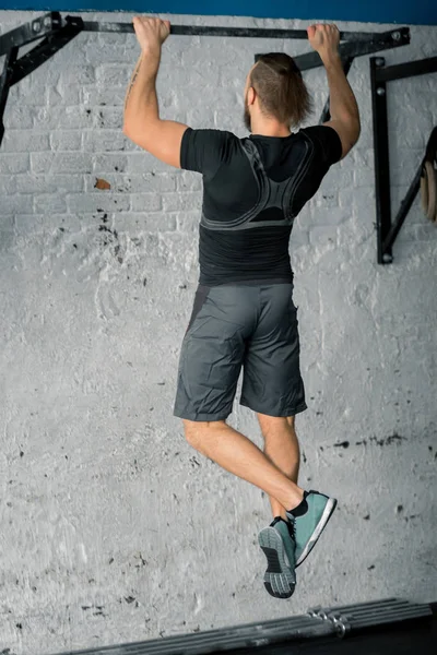 Idrottare muskulös fitness hane modell drar upp på horisontell bar i ett gym — Stockfoto