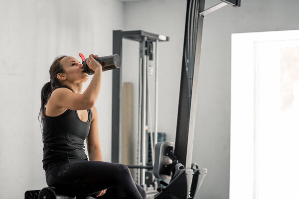 Girl drinking water in gym after workout