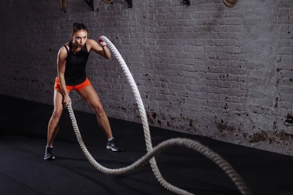 Athletic woman doing battle rope exercises at gym