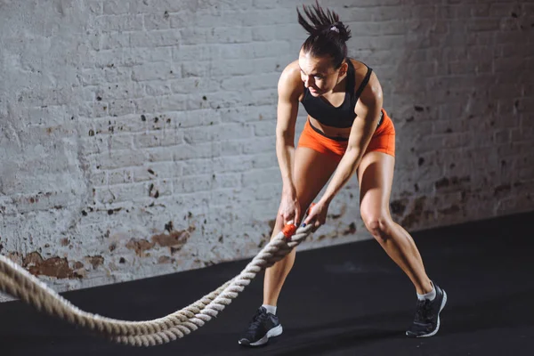Battle ropes session. Attractive young fit and toned sportswoman training in gym