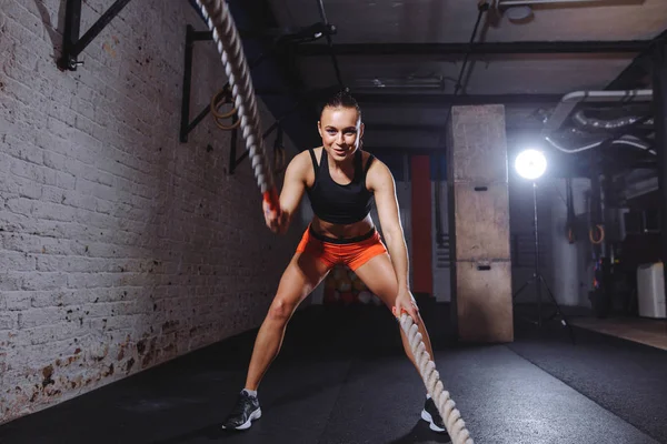 Mujer joven haciendo ejercicio con cuerdas de batalla en el gimnasio de cross fit —  Fotos de Stock