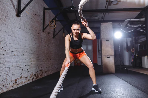 Attractive young fit and toned sportswoman working out with battle ropes — Stock Photo, Image