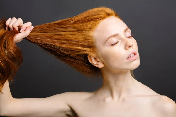 Rossa donna che tiene i capelli sani e lucidi, grigio studio — Foto Stock