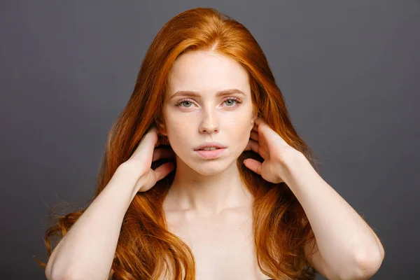 Redhead woman holding her healthy and shiny hair, studio grey — Stock Photo, Image