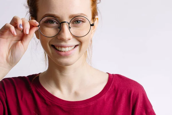 Pelirroja sonriente mujer vistiendo camisa roja mantenga gafas sobre fondo blanco — Foto de Stock