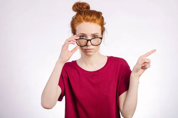 Rousse femme dans des lunettes pointant doigt vers copyspace sur fond blanc — Photo