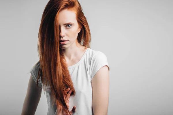 Jovem menina ruiva bonita com sardas olhando para a câmera sorrindo tocando o cabelo — Fotografia de Stock