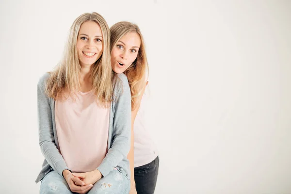 Verrast meisje kijkend naar haar zus twin op witte achtergrond — Stockfoto