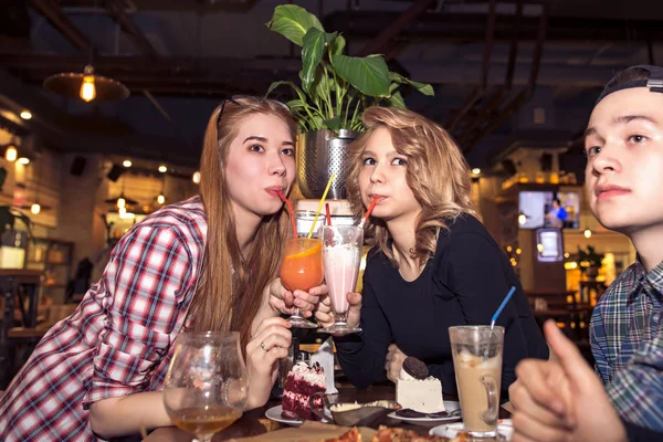 Mujer joven bebiendo batido mientras está sentada con amigos en la cafetería — Foto de Stock