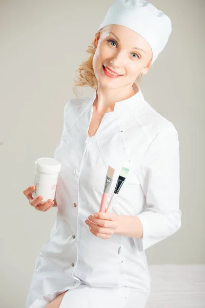 Cosmetologist profissional positivo está segurando escova e tigela . — Fotografia de Stock