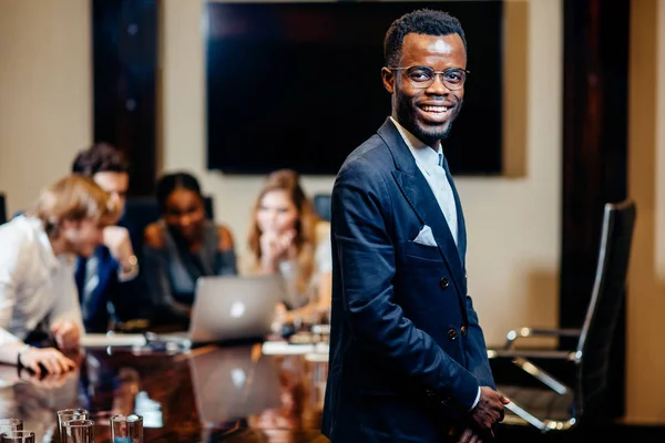 Empresário africano olhando para a câmera com grupo de empresários em segundo plano — Fotografia de Stock