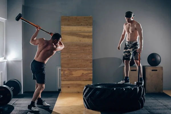 Slägga däck träffar män träning på gym med hammare och traktor däck — Stockfoto