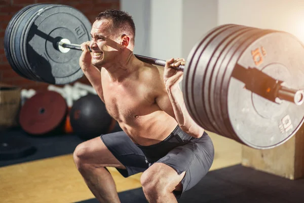 Musculoso hombre entrenamiento sentadillas con barras en los hombros —  Fotos de Stock