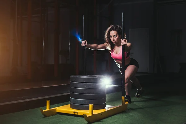 Fêmea empurrando o equipamento de exercício prowler em relva artificial — Fotografia de Stock