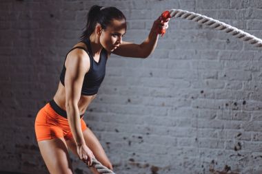 woman training with battle rope in cross fit gym