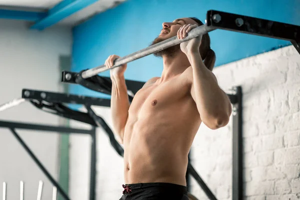 Atleta muscular fitness modelo masculino tirando hacia arriba en la barra horizontal en un gimnasio — Foto de Stock