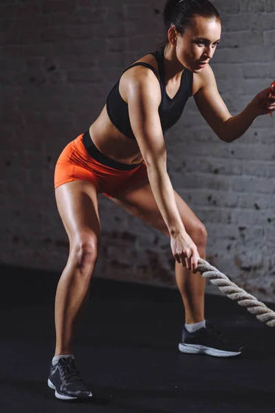 Athletic woman doing some cross fit exercises with battle rope indoor — Stock Photo, Image