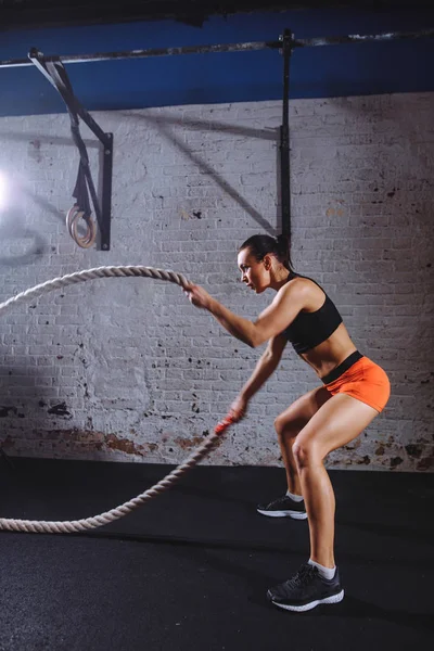 Mujer atlética haciendo algunos ejercicios de cross fit con cuerda de batalla interior — Foto de Stock