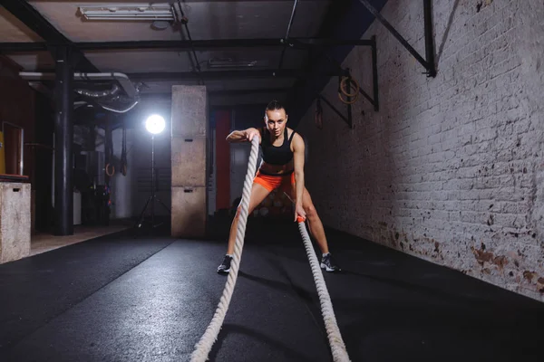Attractive young fit and toned sportswoman working out with battle ropes — Stock Photo, Image