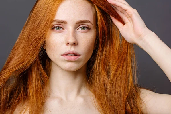 redhead woman holding her healthy and shiny hair, studio grey