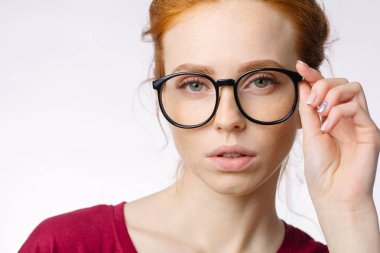 Kızıl saçlı gülümseyen kadın kırmızı gömlek giymiş beyaz arka plan üzerinde gözlük tutun