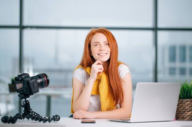 Bilgisayarı ve kitabı olan genç bir kadın blogcu kameraya bakıyor.