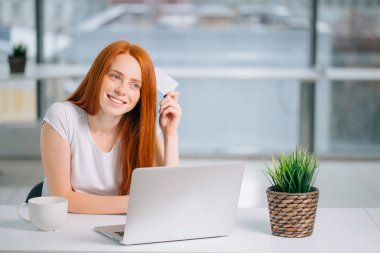 Elinde kredi kartıyla ne alacağına karar veren mutlu kızıl saçlı müşteri.