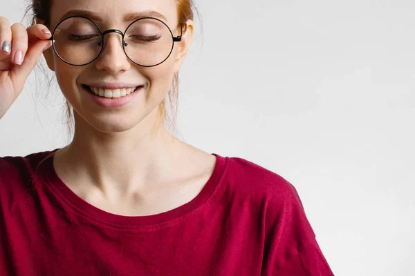 Pelirroja sonriente mujer vistiendo camisa roja mantenga gafas sobre fondo blanco —  Fotos de Stock